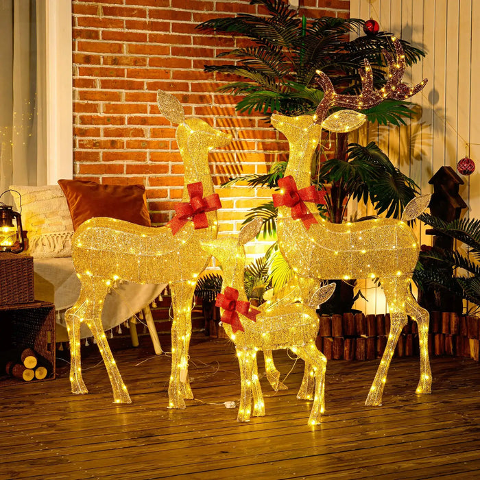 Christmas outdoor decor with three illuminated golden reindeer sculptures wearing red bows on a wooden deck