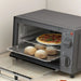 Gray toaster oven with pizza and bread inside on a light-colored surface.
