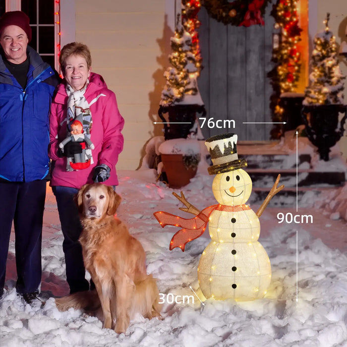 Couple with golden retriever dog and illuminated snowman decoration with red scarf and black top hat in snowy front yard
