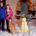 Couple with golden retriever dog and illuminated snowman decoration with red scarf and black top hat in snowy front yard