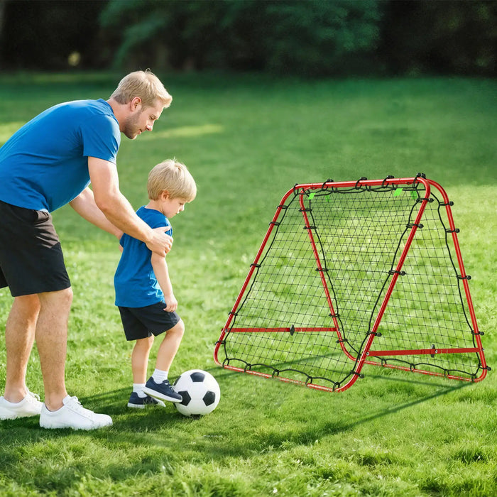 Father teaching young boy to kick soccer ball into portable red rebounder net on grass field