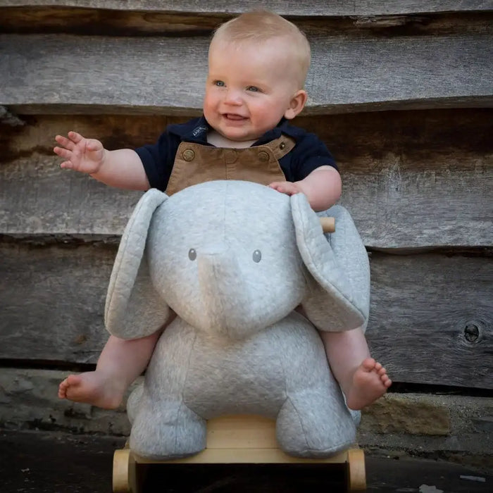 Baby sitting on a plush elephant toy against a wooden background