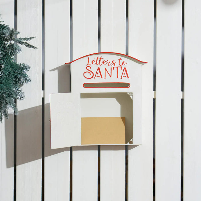 White wooden mailbox with red text "Letters to Santa" on white fence, containing a brown envelope
