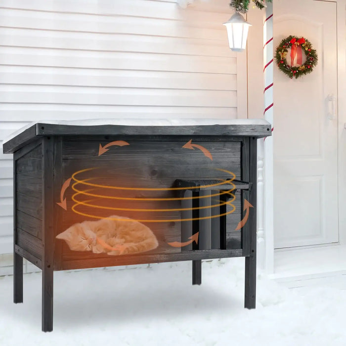 Grey outdoor insulated cat house with a sleeping orange kitten inside on snowy porch with wreath