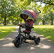 Children's tricycle with a red seat and black frame on a paved path in a park.