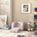 Kids playroom with pink unicorn-themed convertible foam chair, teddy bear, books, and floral wall art