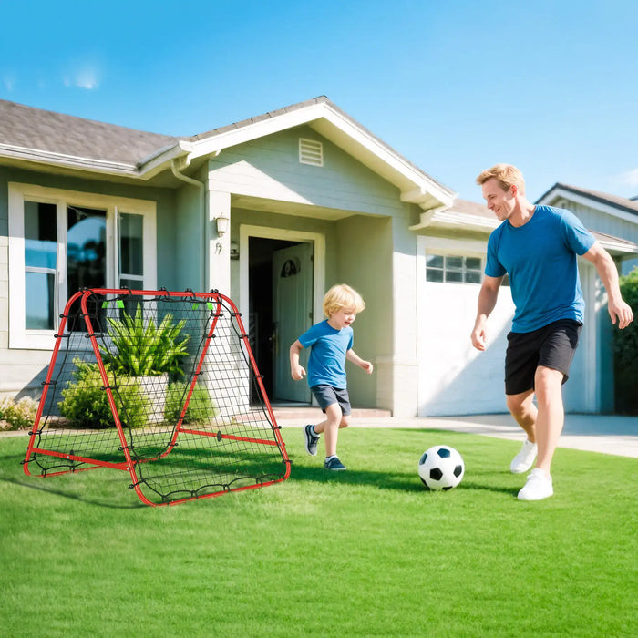 Father and son playing soccer on green lawn outside suburban house with red rebounder net
