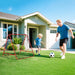Father and son playing soccer on green lawn outside suburban house with red rebounder net