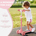 Toddler girl riding pink three-wheeled scooter on pathway in park, outdoor kids gift