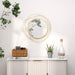 Decorative wall mirror with circular design on a white wall above a cabinet with plants and a bottle.