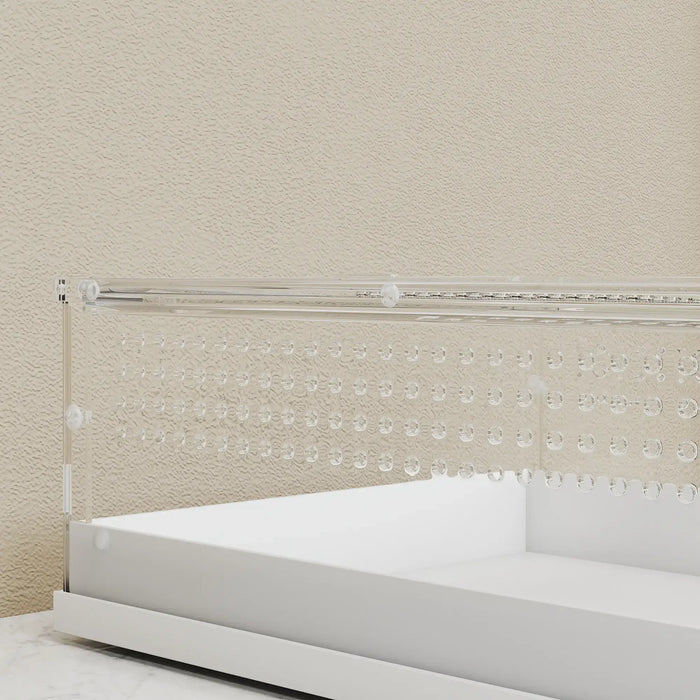 Clear crib safety fence with white mattress against a beige wall