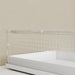 Clear crib safety fence with white mattress against a beige wall