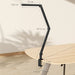 Black adjustable desk lamp on a wooden table with measurements indicated.