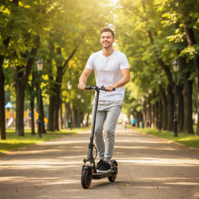 Young man riding black electric scooter with pneumatic tyres on tree-lined park path in daylight