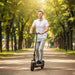 Young man riding black electric scooter with pneumatic tyres on tree-lined park path in daylight