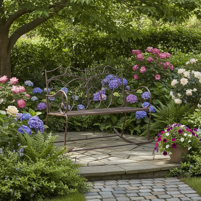 Antique brown wrought iron rocking garden bench on stone patio surrounded by blooming roses and hydrangeas