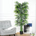 Artificial bamboo plant in a living room setting with a gray sofa and white walls.