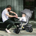Man interacting with a child in a stroller outdoors.