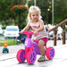 Toddler riding a violet and fuchsia baby balance bike with four rubber wheels outdoors