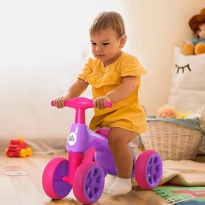 Baby riding violet and fuchsia balance bike with four rubber wheels in playroom