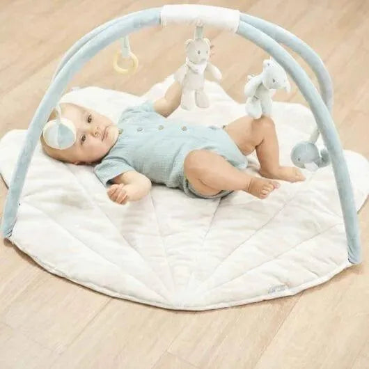 Baby lying on padded playmat with arches, hanging toys, and soft animal rattles