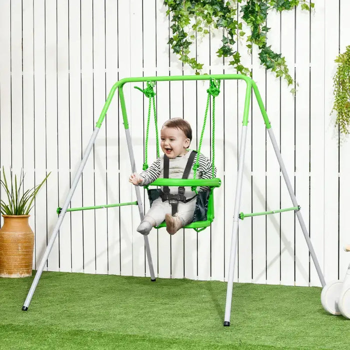 Baby in green toddler swing with safety belt, indoor outdoor setting, white fence background