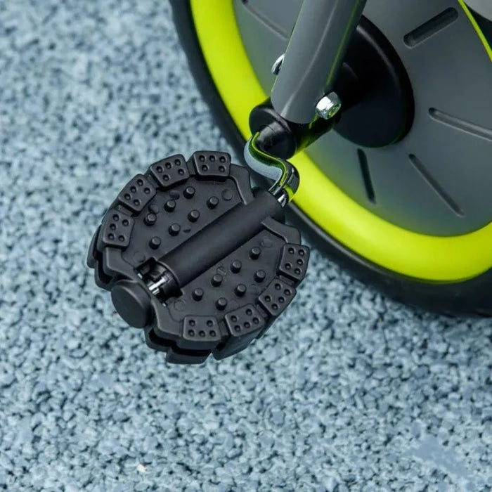 Close-up of black baby trike front wheel with textured pedal and green rim on blue surface