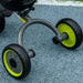 Close-up of baby trike rear wheels with green accents on textured outdoor surface