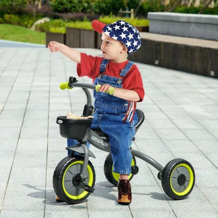 Toddler riding black trike with green wheels and adjustable seat outdoors, wearing star cap