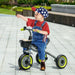 Toddler riding black trike with green wheels and adjustable seat outdoors, wearing star cap
