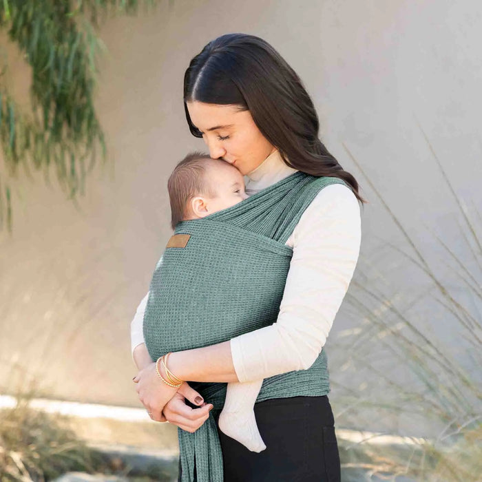 Woman holding a baby in a green sling against a natural background