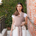 Woman carrying a baby in a beige woven carrier against a brick wall.