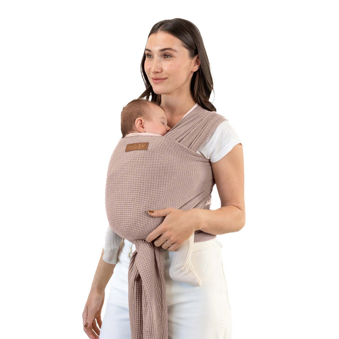 Woman holding a baby in a brown woven baby carrier against a white background