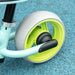 Close-up of green EVA wheel on balance bike with adjustable seat, blue textured surface