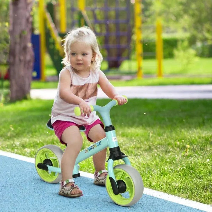 Toddler riding a mint green balance bike with EVA wheels outdoors on a sunny day
