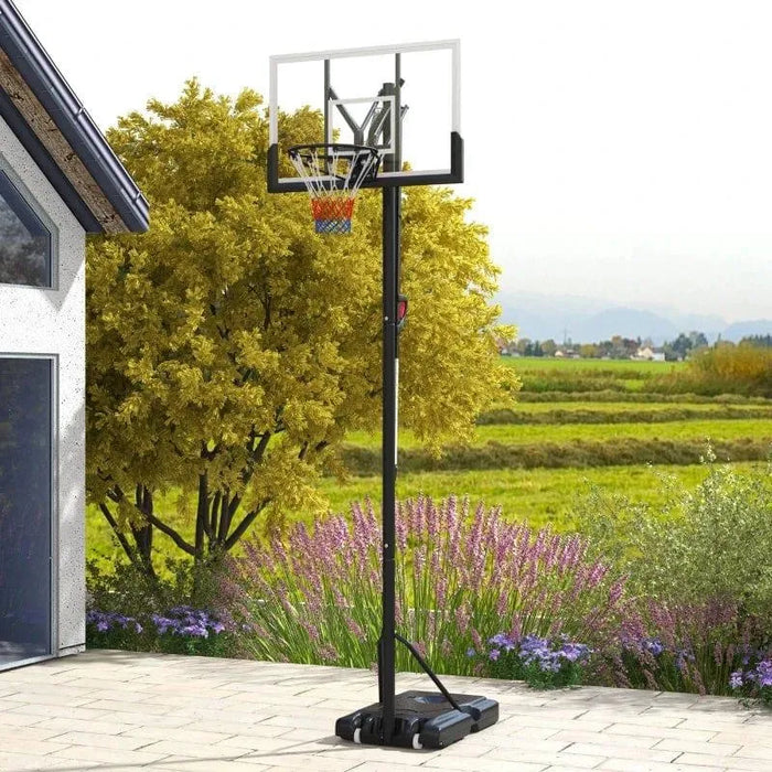 Adjustable outdoor basketball stand with clear backboard on patio near garden and fields