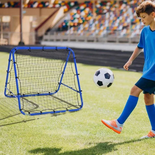 Boy kicking soccer ball at blue football rebounder net on grass sports field