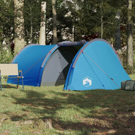 Blue taffeta camping tent for 4 persons set up in a forest clearing with a chair nearby