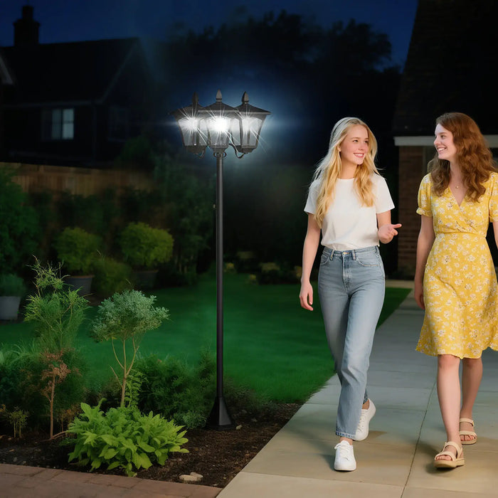 Two women walking on a garden pathway at night with bright black metal lamp post lighting the path