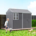Boy playing soccer in backyard with gray metal garden shed and small dog on grass
