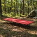 Red portable folding camping bed with steel frame in forest campsite setting