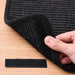 Hand lifting black woven mat with Velcro backing on wood surface, included extra Velcro strip