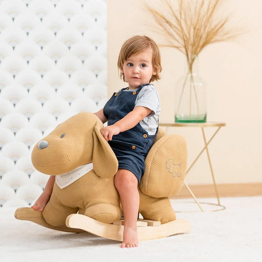 Toddler on caramel dog rocker toy with safety harness in bright nursery setting