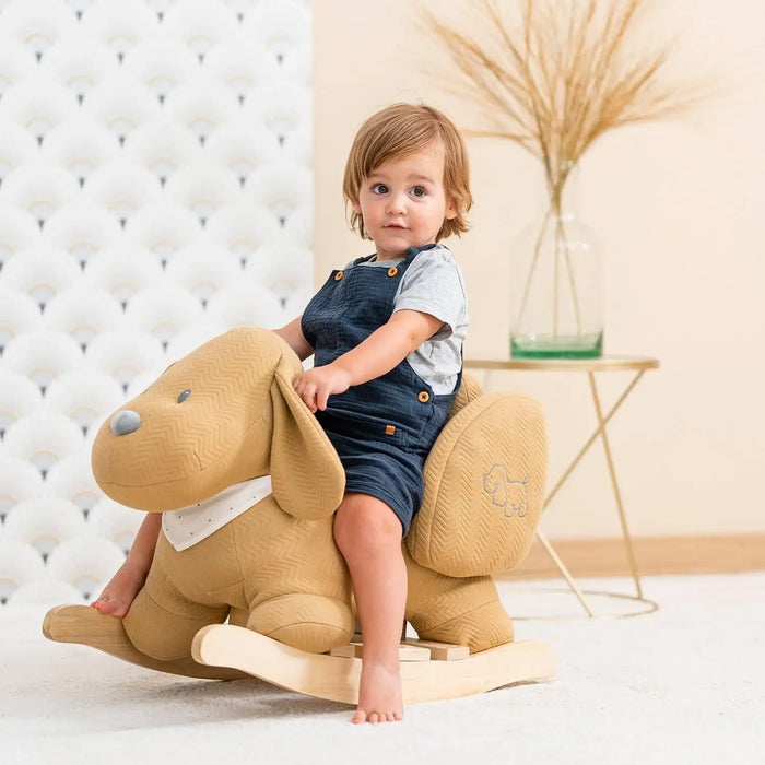 Toddler on caramel dog rocker toy with safety harness in bright nursery setting
