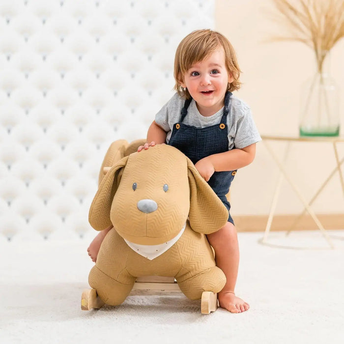 Smiling toddler on caramel dog rocker toy with safety harness in a modern nursery