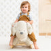 Toddler riding plush dog rocker with safety harness in bright, modern nursery setting