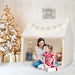 Mother and daughter by beige indoor play tent with star lights, Christmas tree and gifts