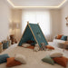 Classic blue kids play tent with wooden poles in cozy playroom, surrounded by pillows and plush toys
