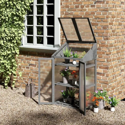 Grey 3-tier wooden mini greenhouse with potted plants on shelves by brick wall