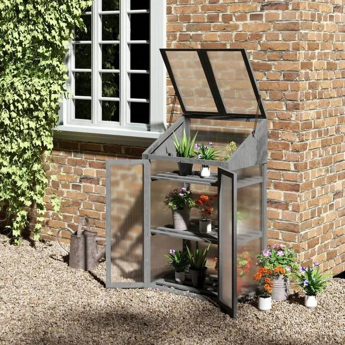 Grey 3-tier wooden mini greenhouse with potted plants on shelves by brick wall